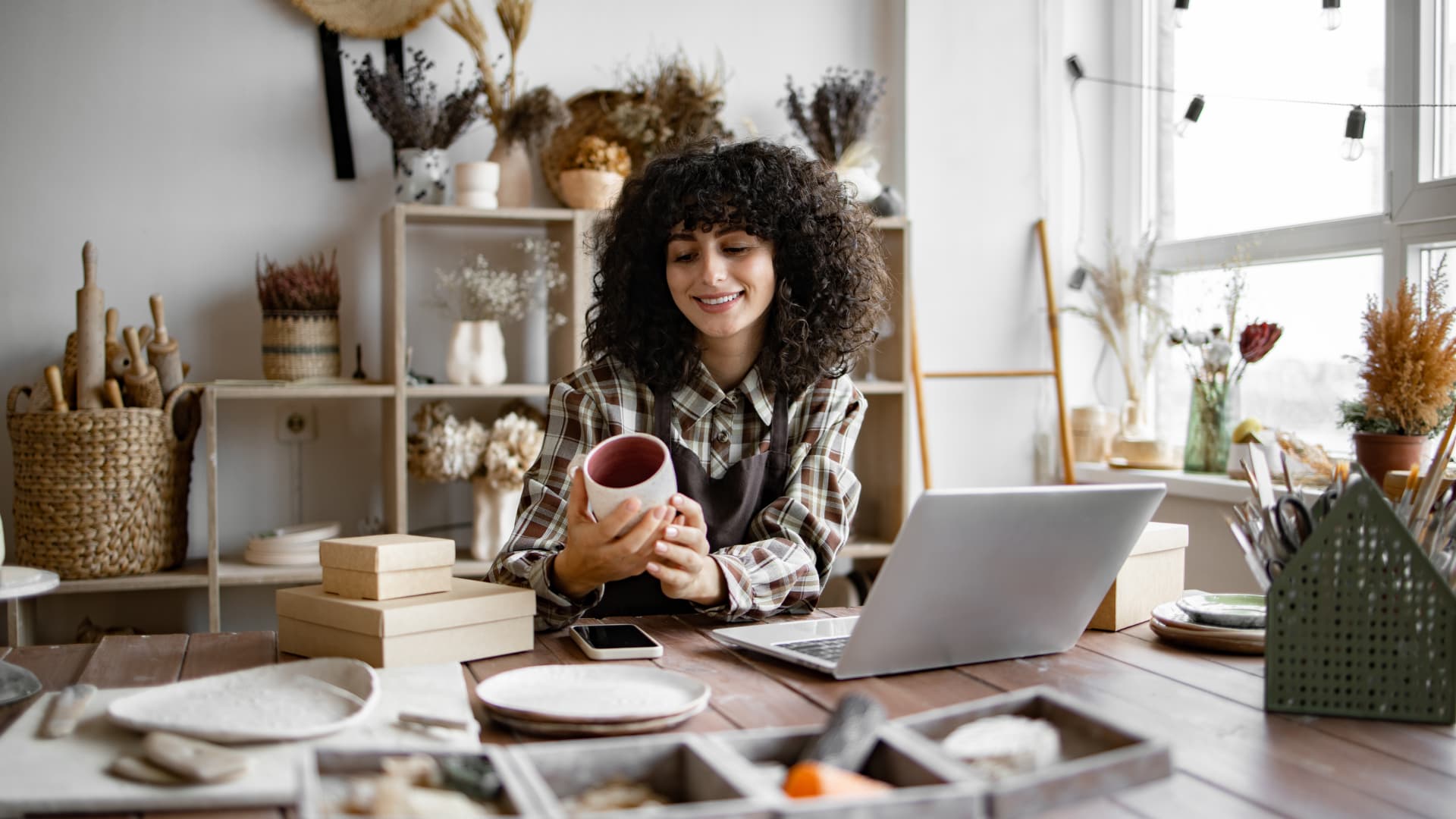 uma mulher segurando uma caneca em frente ao notebook